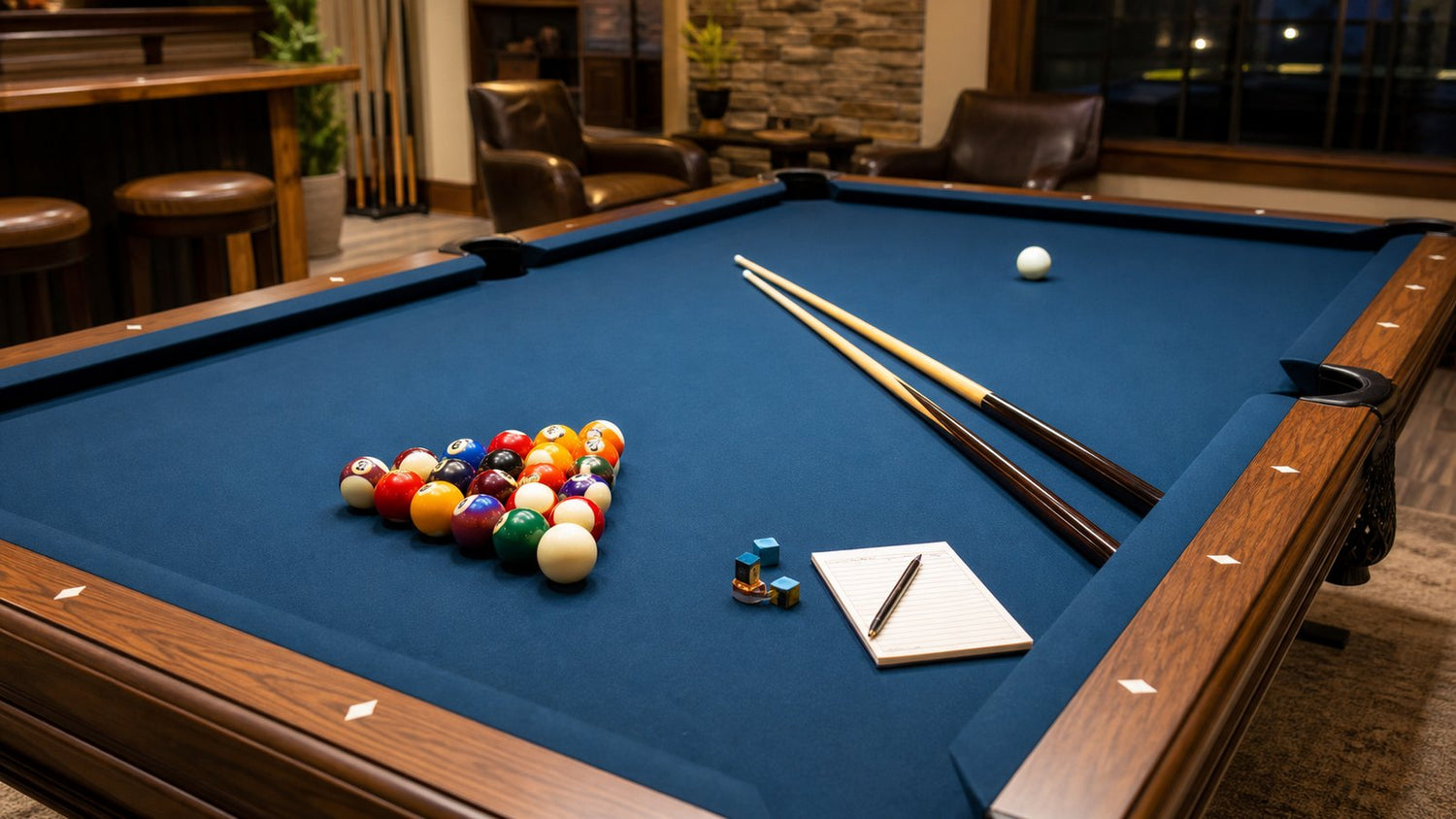 Pool table set up with racked balls, cues, chalk, and a score pad for game night