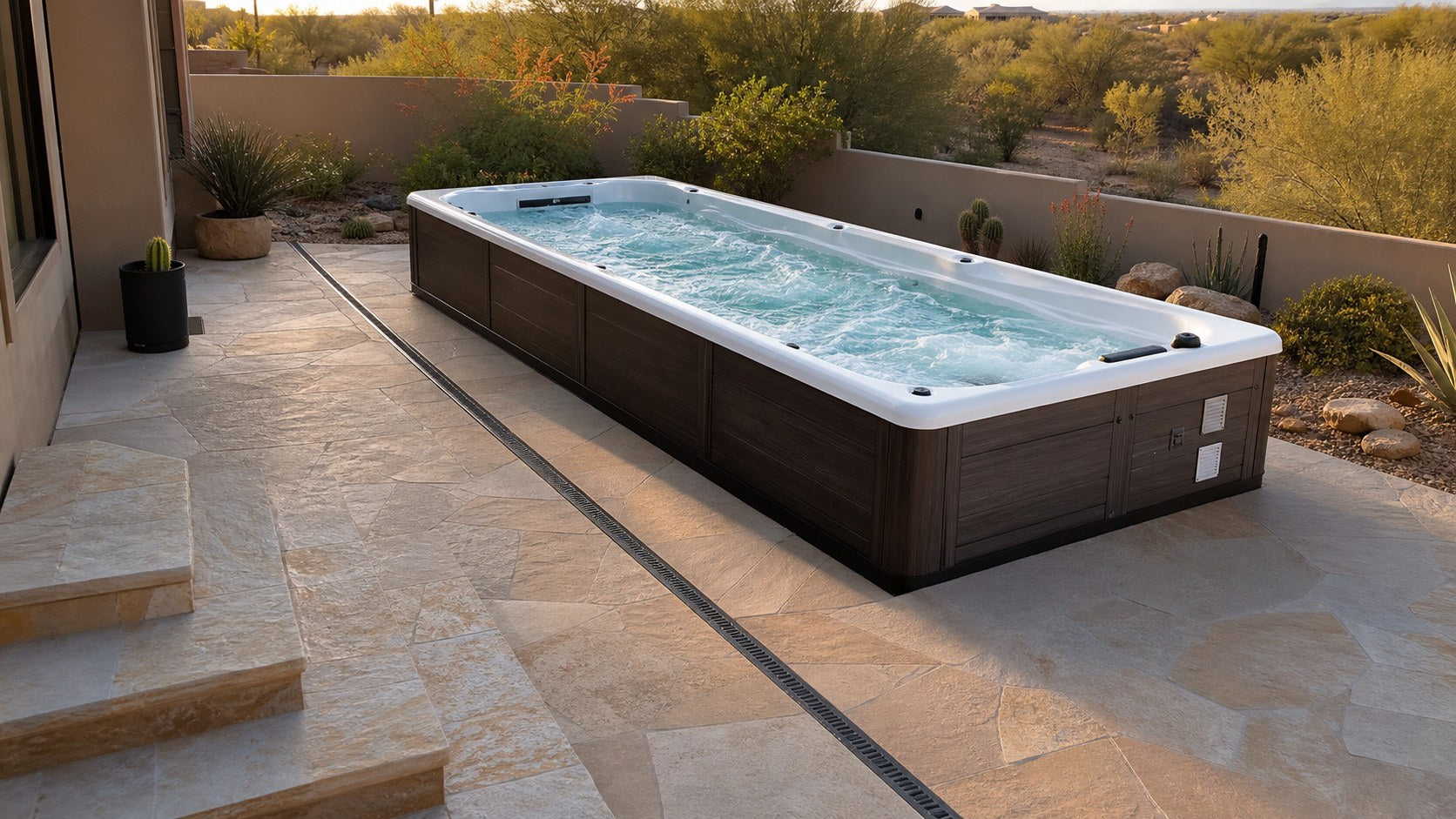 Swim spa on a sloped stone patio with a linear drain, entry steps, and clear equipment access